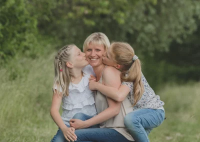 Zwei Töchter geben ihrer Mama einen herzlichen Kuss in einem emotionalen Familienfotoshooting.